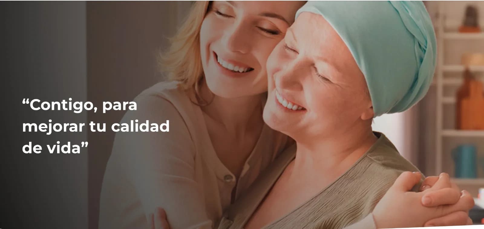 Dos mujeres se abrazan sonriendo, una de ellas con un pañuelo en la cabeza, junto al rótulo «Contigo, para mejorar tu calidad de vida»